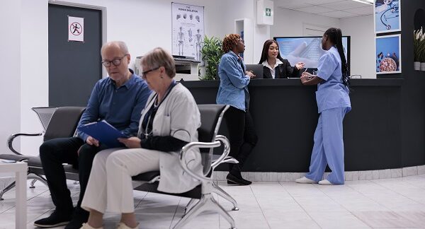 en un de los centros de salud, hay en la sala de espera una doctora explicándole los resultados del examen al paciente, meintras la recepcionista habla con una enfermera y un hombre